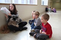 high school students reading their stories to elementary students in hallway