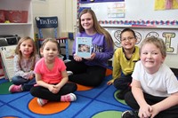 one high school student smiling with book and four elementary students