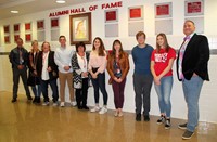 honorees and student tour guides standing in front of alumni hall of fame wall