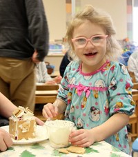 student standing next to gingerbread house