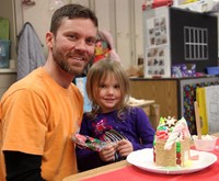 two people smiling next to gingerbread house