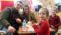 four people smiling next to gingerbread house