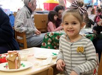 student smiling next to gingerbread house