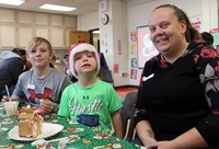 three people smiling next to gingerbread house