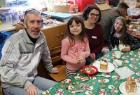 four people smiling next to gingerbread house