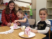 three people smiling next to gingerbread houses