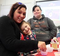 three people smiling next to gingerbread house