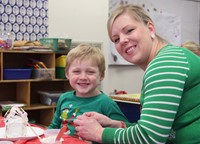 two people smiling next to gingerbread house