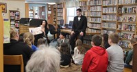 wide shot of theatre guild member reading book to library guests