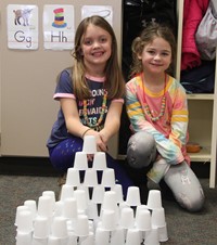 students sitting next to tower made from 100 cups