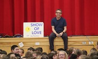 presenter sitting next to show of love sign smiling