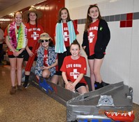 six students standing with their cardboard boat