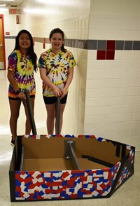 two students standing with their cardboard boat