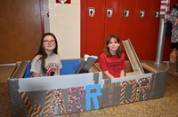 two students sitting in their cardboard boat