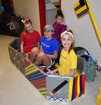 three students sitting in their cardboard boat