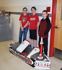 three students standing with their cardboard boat