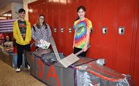 three students standing with their cardboard boat