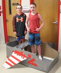 two students standing with cardboard boat