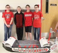 four students standing with cardboard boat