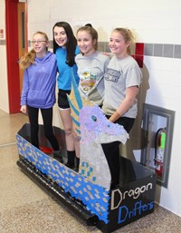 four students standing with cardboard boat