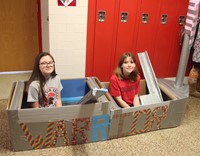 two students sitting in cardboard boat