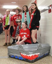 five students standing with cardboard boat
