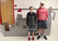 two students standing with cardboard boat