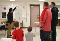 students and adults watching rube goldberg machine demonstration