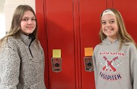 two students smiling next to lockers with positive post it notes