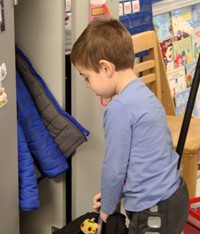 student putting backpack into cubby