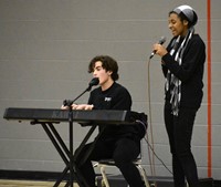 person singing and person playing piano and singing at big gifted give event