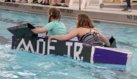 two students paddling boat back to start