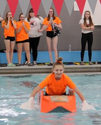 student paddling boat with team cheering them on in background