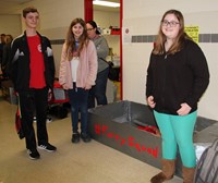 three students standing next to boat