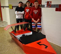 three students standing next to boat