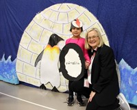 student and teacher smiling next to backdrop with penguin