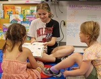 high school student reading to kindergarten students