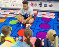 high school student reading to kindergarten students