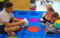 high school student reading to kindergarten students